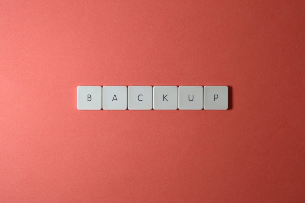 Close-up of keyboard keys spelling 'BACKUP' placed on a coral-colored surface.